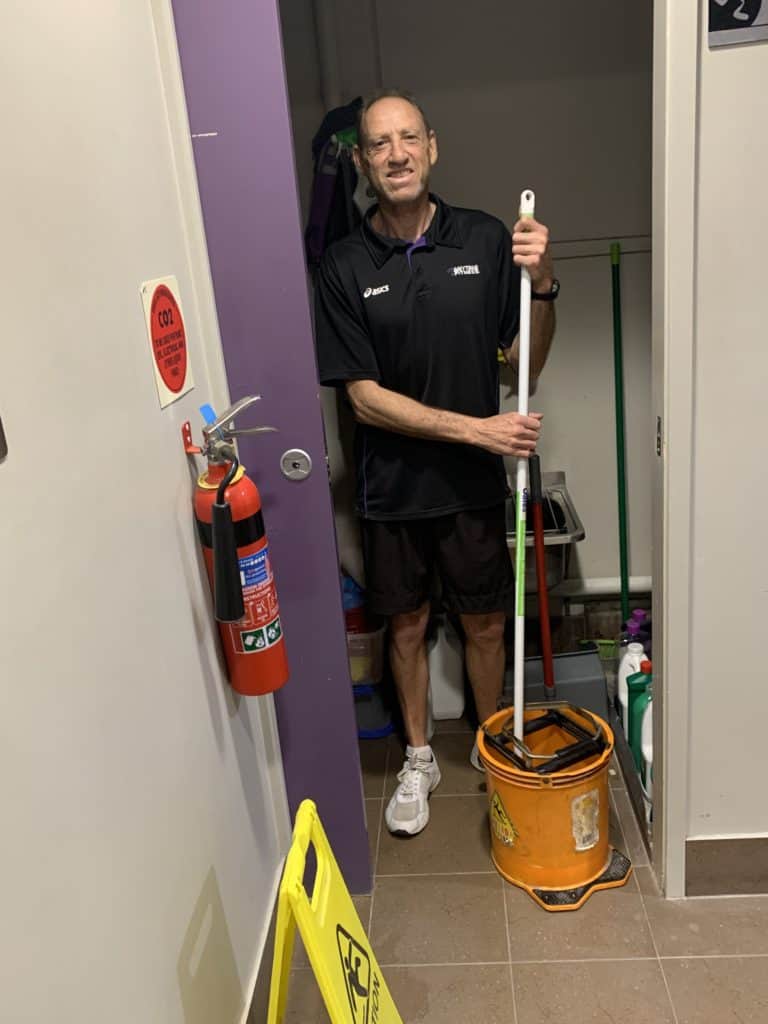 Employee James stands with a mop and bucket in the doorway of a cleaning closet at Anytime Fitness Tweed
