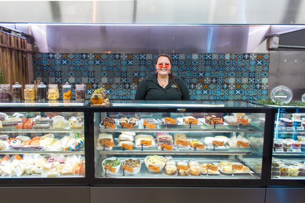 Gabrielle behind the counter, under the counter is the wide selection of The Deli's food menu.