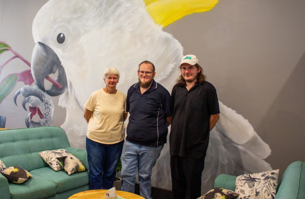 Gwenda standing smiling with her newfound Cockatoo Cafe family.
