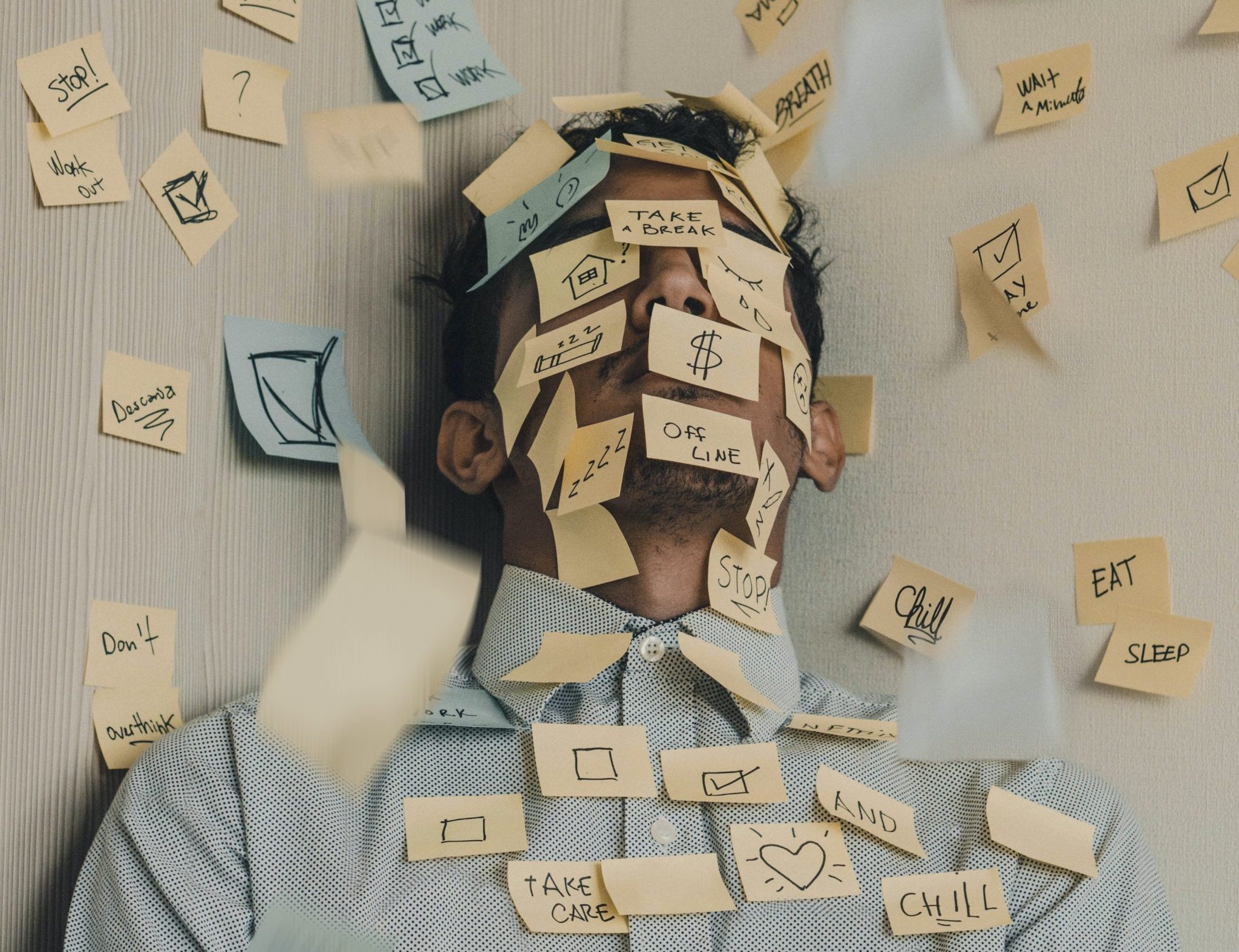 Stressed man covered in sticky notes reminding him to relax.