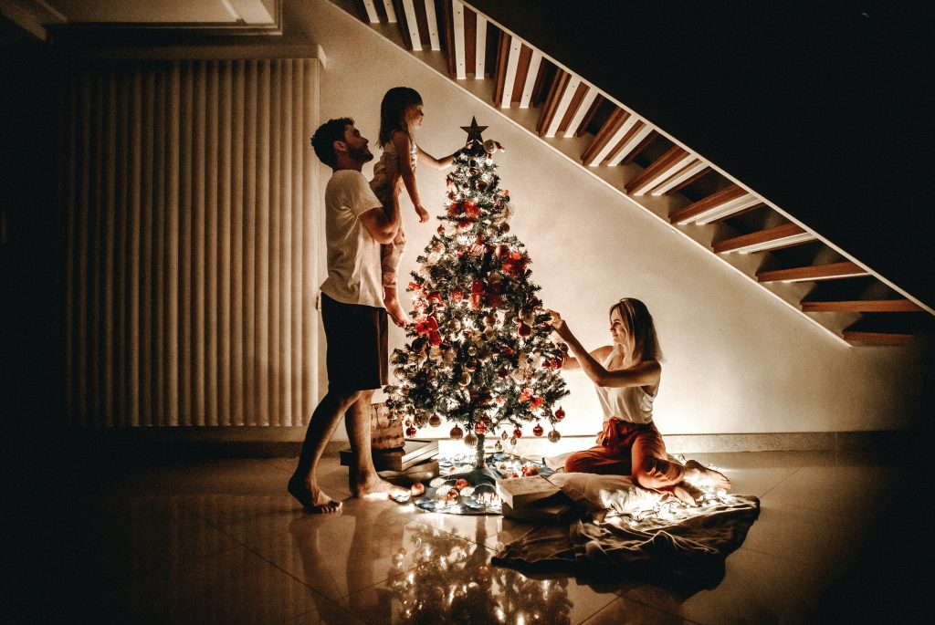 A family putting up a Christmas tree in their living room, illuminated by Christmas lights.