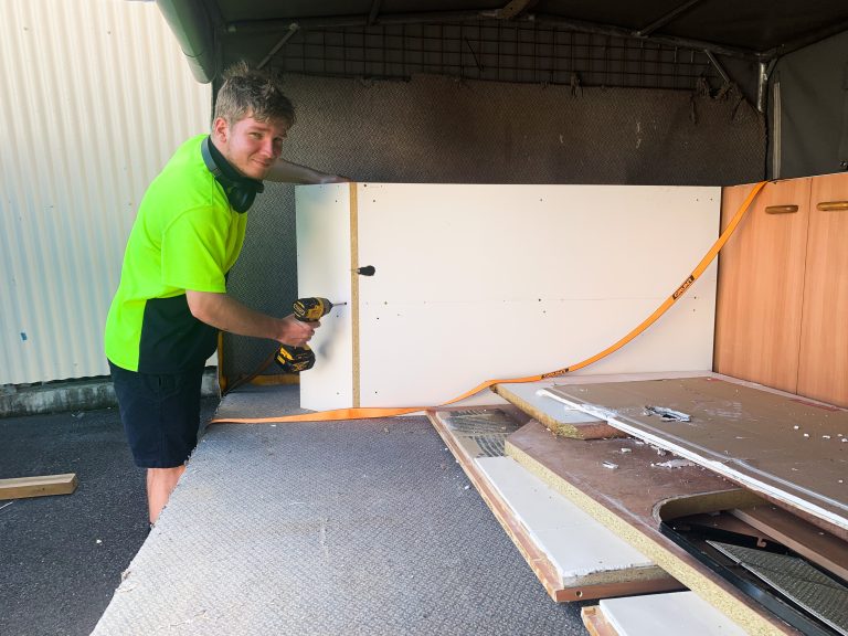 Xander putting together a cabinet, flashing the camera a grin.