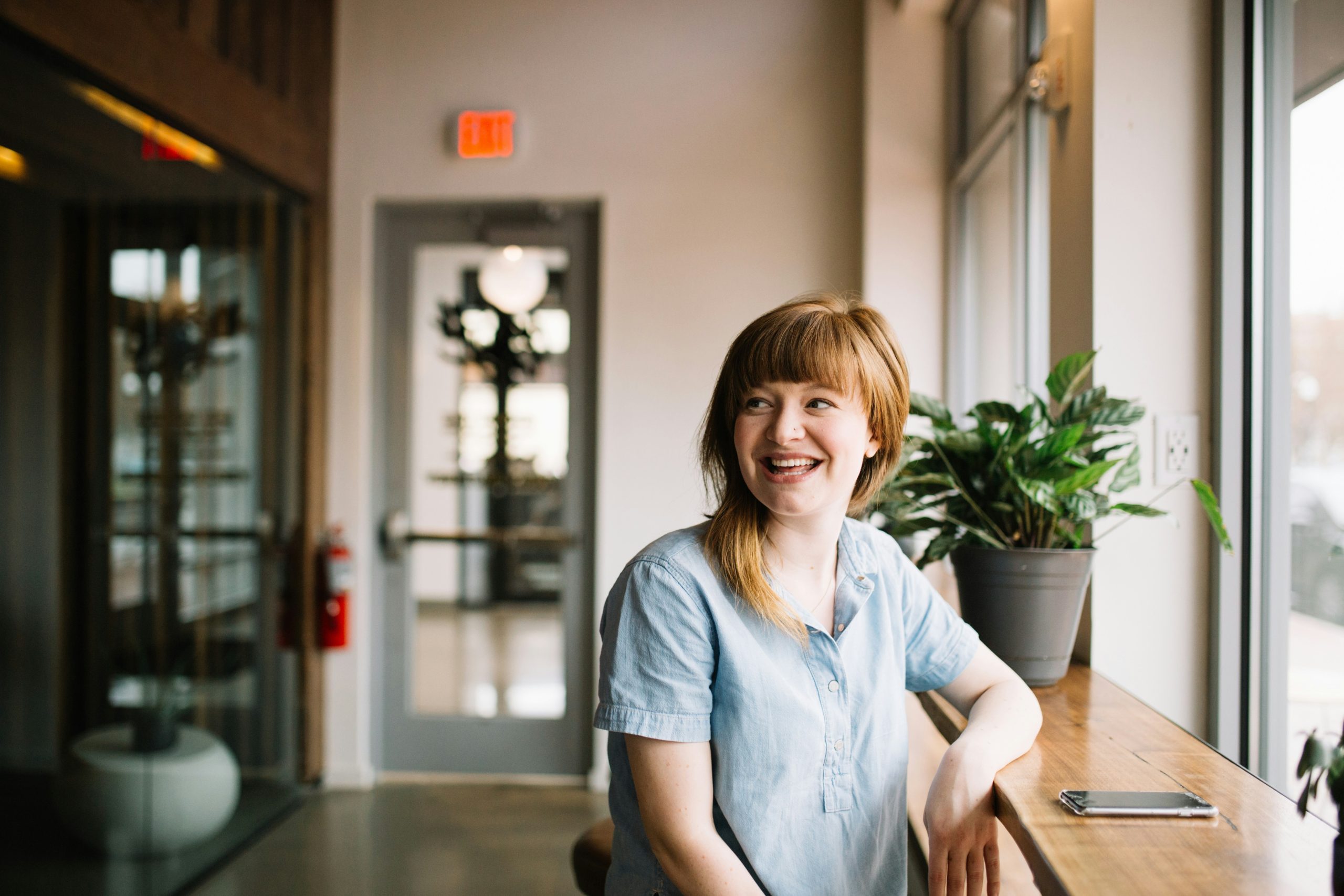A redheaded woman sitting at a desk and giving a wide smile
