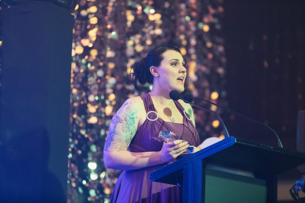 A women in a purple dress stands at a lectern speaks after receiving an award