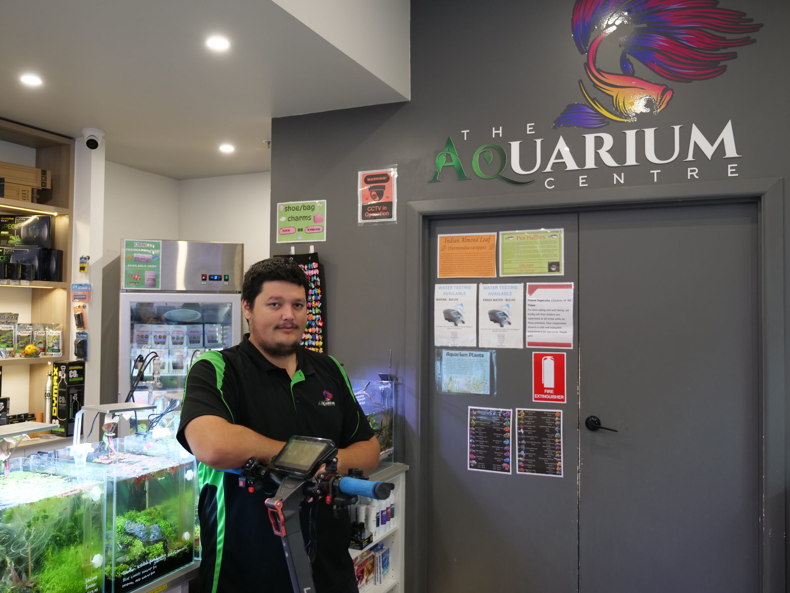 Darcy standing below the signage of The Aquarium Centre in front of some colourful fish tanks.